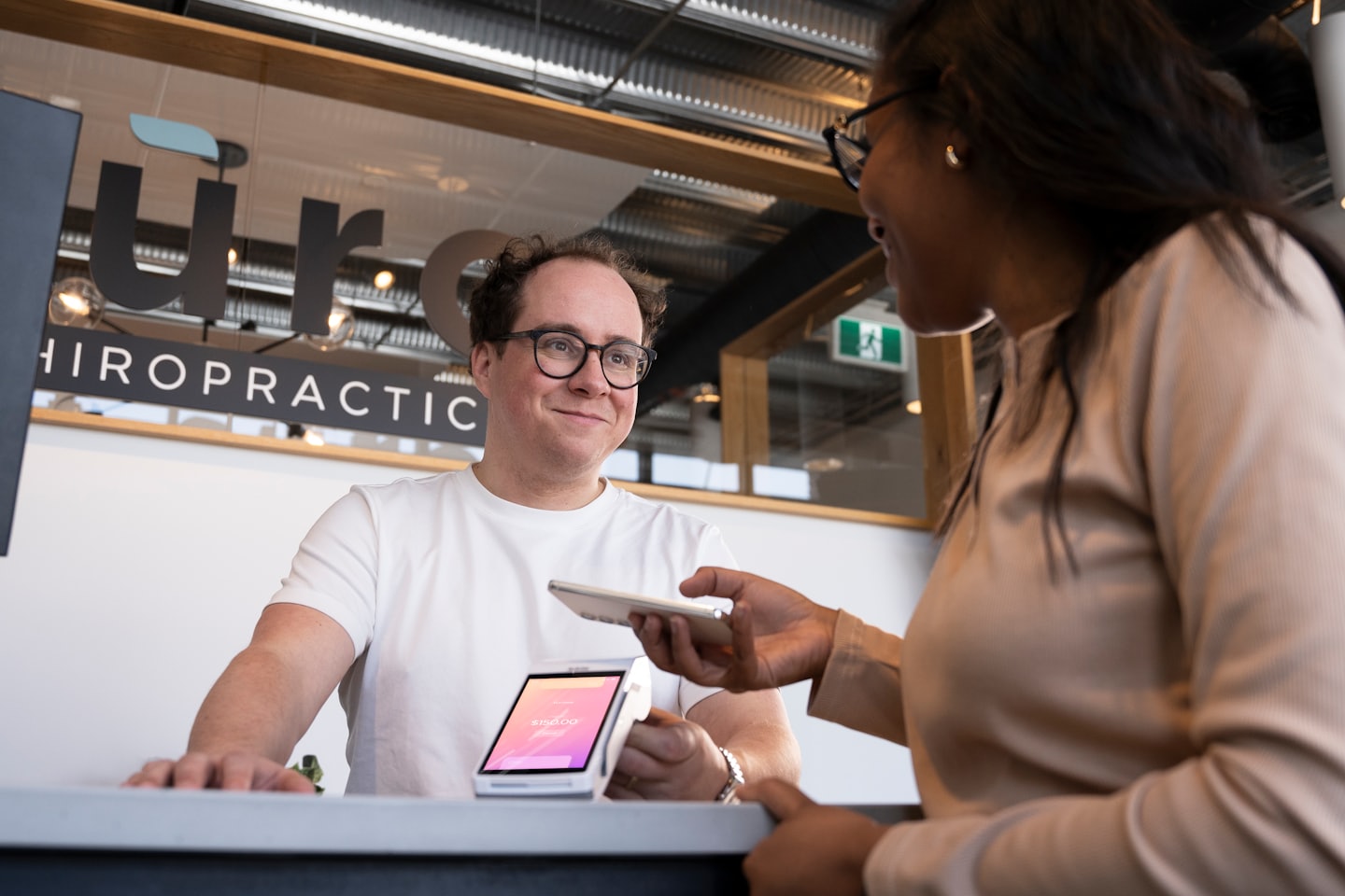 Staff member smiles as customer pays with smartphone at reception.